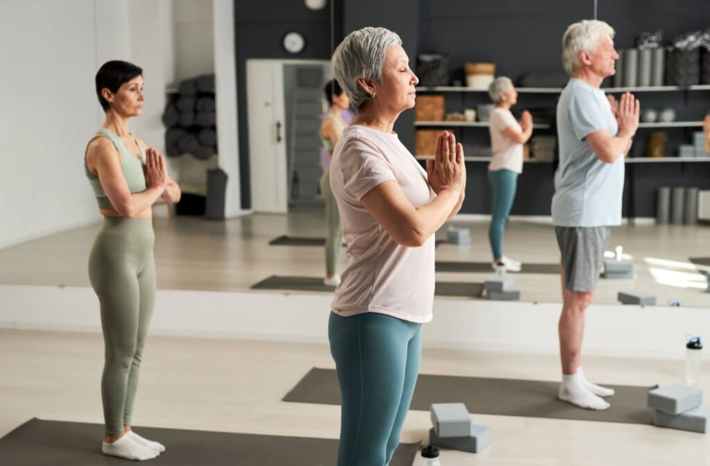A group of seniors standing and meditating during a yoga class at an independent living community.